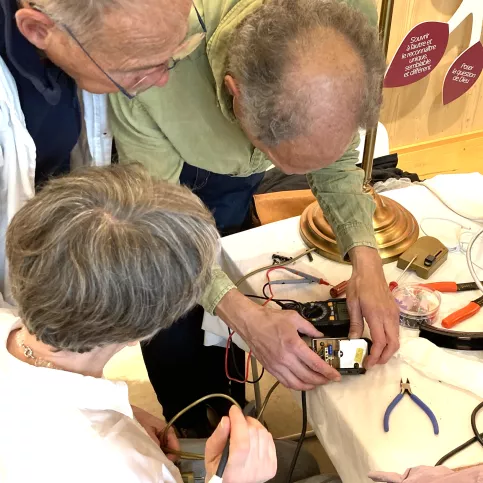 trois personnes penchées en train de réparer un objet electronique